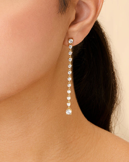 Close-up of a person wearing a set of dangling earrings with clear stones.