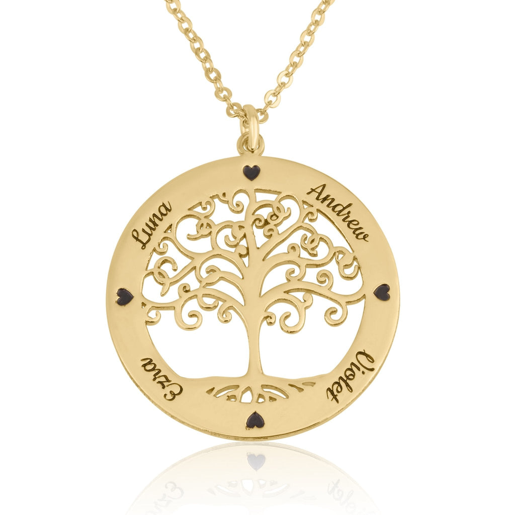A gold family tree pendant necklace on a white background. The circular pendant features a cutout tree design with the names of family members engraved on the outer ring, including Luna, Andrew, Ezra, and Violet, accented by small black heart-shaped stones.